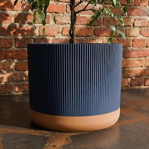 Peut inclure: Un pot de fleurs cylindrique présentant une section supérieure bleu marine profond avec une texture côtelée verticale et une base lisse de couleur terre cuite. Le pot est de forme circulaire et contient une petite plante verte.