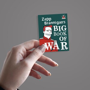 May include: A rectangular sticker featuring the character Zapp Brannigan from Futurama. The sticker has a teal background with the text "Zapp Brannigan's BIG BOOK OF WAR" and an illustration of Zapp in his red uniform.