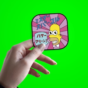 May include: A square sticker featuring Homer Simpson with Japanese text. The sticker has a pink and purple background with Homer's face in the center. The text includes "Mr. Sparkle" and other Japanese phrases. The sticker is held against a bright green background.