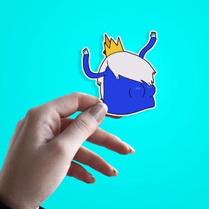 Pode incluir: Um autocolante de desenho animado azul de uma personagem com barba branca, coroa de ouro e braços levantados. O autocolante é segurado contra um fundo turquesa brilhante.