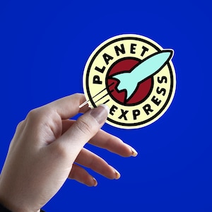 Peut inclure: Un autocollant rond avec l'inscription "PLANET EXPRESS" encerclant un cercle rouge avec une fusée bleu clair. L'autocollant est tenu sur un fond bleu.