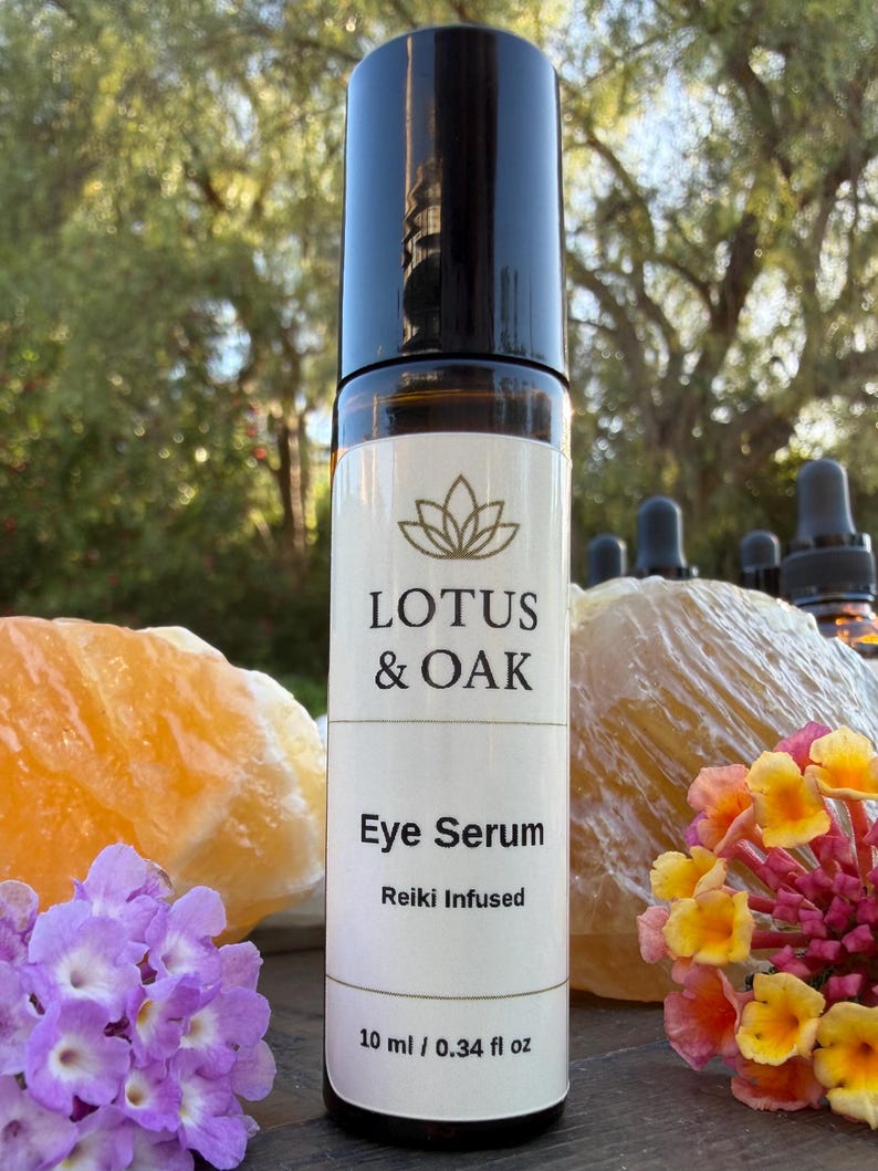 Może przedstawiać: Brązowa szklana butelka z czarną nakrętką, z napisem "LOTUS & OAK Eye Serum Reiki Infused". Butelka zawiera 10 ml / 0,34 fl oz. Tło obejmuje pomarańczowe i ż&oacute;łte kryształy, fioletowe i ż&oacute;łte kwiaty oraz rozmyte zielone drzewo.