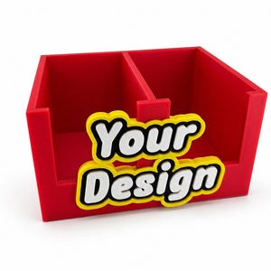 Può includere: Un organizer da scrivania rosso acceso con due scomparti. Presenta la scritta "Your Design" in bianco con un contorno giallo. L'articolo è realizzato in materiale solido e si trova su una superficie bianca.