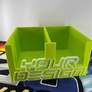 May include: A lime green, two-compartment organiser with the text "YOUR DESIGN" in white, outlined in lime green. The organiser is made of a solid material and sits on a patterned surface.