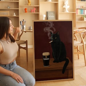 K&ouml;nnte beinhalten: Gerahmtes Kunstwerk mit einer schwarzen Katze, die eine Zigarette raucht, und einem Pint Guinness. Die Katze hat gelbe Augen und sitzt auf einer Holzoberfl&auml;che vor einem dunkelroten Hintergrund. Das Kunstwerk ist in einem Holzrahmen.