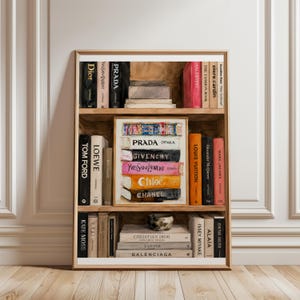 Könnte beinhalten: Ein gerahmter Wandkunstdruck, der ein hölzernes Bücherregal voller moderelevanter Bücher zeigt. Die Buchrücken tragen Markennamen wie Dior, Prada, Tom Ford, Loewe, Louis Vuitton, Givenchy, Yves Saint Laurent, Chloe, Chanel und Balenciaga.