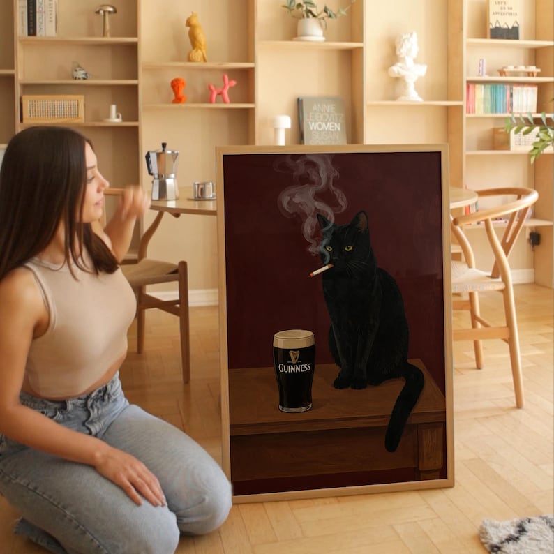 K&ouml;nnte beinhalten: Gerahmtes Kunstwerk mit einer schwarzen Katze, die eine Zigarette raucht, und einem Pint Guinness. Die Katze hat gelbe Augen und sitzt auf einer Holzoberfl&auml;che vor einem dunkelroten Hintergrund. Das Kunstwerk ist in einem Holzrahmen.