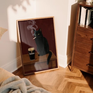 K&ouml;nnte beinhalten: Gerahmter Kunstdruck mit einer schwarzen Katze, die eine Zigarette raucht, neben einem Pint Guinness. Das Kunstwerk hat einen dunkelroten Hintergrund und ist in einem Holzrahmen pr&auml;sentiert.