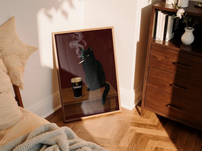 K&ouml;nnte beinhalten: Gerahmter Kunstdruck mit einer schwarzen Katze, die eine Zigarette raucht, neben einem Pint Guinness. Das Kunstwerk hat einen dunkelroten Hintergrund und ist in einem Holzrahmen pr&auml;sentiert.