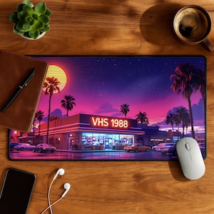 Può includere: Tappetino per mouse rettangolare con un'illustrazione retrò di un edificio con la scritta "VHS 1988" sotto un cielo al tramonto con palme. La tavolozza dei colori include sfumature di viola, rosa e arancione.