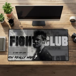 Puede incluir: Una alfombrilla de escritorio rectangular con un gráfico en blanco y negro de un hombre fumando, con el texto en negrita FIGHT CLUB y la frase IS THIS THE LIFE YOU REALLY WANT? impresos en la superficie en un estilo monocromático.