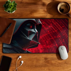 Könnte beinhalten: Schwarzes und rotes Mauspad mit einer detaillierten Illustration von Darth Vaders Helm. Das Design hat einen Drahteffekt, vor einem roten Hintergrund mit radialen Linien. Eine weiße Maus, ein Smartphone und eine Tasse Kaffee liegen auf einer Holzoberfläche.