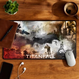 Può includere: Un tappetino per mouse Titanfall rettangolare con una scena di battaglia con soldati e veicoli futuristici in tonalità di grigio, arancione e bianco. La parola "TITANFALL" è stampata in bianco in basso. Un mouse bianco, un telefono e una tazza di caffè sono su una superficie di legno.