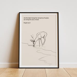 May include: Framed art print with a minimalist line drawing of a deer drinking water. The artwork includes the text "As the deer longs for streams of water, so I long for you, O God. Psalm 42:1" in black font on a beige background.