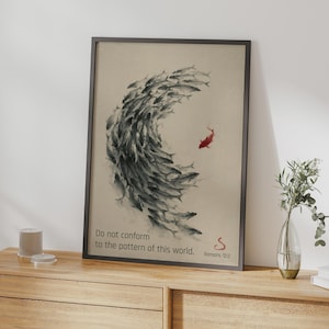 Può includere: Una stampa artistica incorniciata raffigurante un grande banco di pesci grigi a forma di mezzaluna che nuotano insieme, con un singolo pesce rosso che nuota nella direzione opposta. Il testo recita: Do not conform to the pattern of this world. Romans 12:2.
