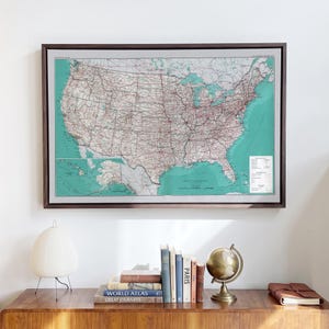 May include: A framed wall map of the United States featuring a teal ocean background, detailed state boundaries, and a network of red transportation lines. The map includes a legend and inset maps of Alaska and Hawaii in a dark wood frame.