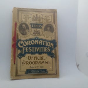 May include: A vintage tan paper programme for the Leeds Coronation Festivities dated June 22nd 1911. The cover features dark blue text, two circular portraits of royalty, a red ribbon binding on the left side, and the publisher name M.C. Morrison Leeds.