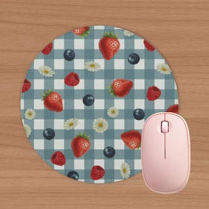 May include: A round mouse pad featuring a blue and white gingham check pattern decorated with a repeating print of red strawberries, raspberries, dark blue blueberries, and small white daisy flowers, paired with a light pink computer mouse.