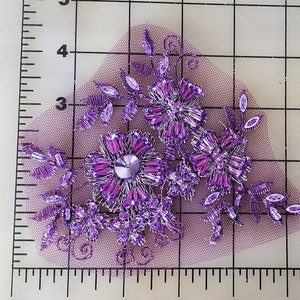 May include: Purple beaded floral applique with a silver metallic thread design on a sheer purple mesh fabric.