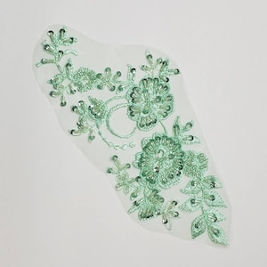 May include: A light green beaded floral applique with a delicate design. The applique is made of sequins and beads and is perfect for adding a touch of elegance to any project.