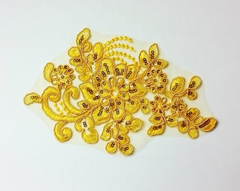 May include: A gold floral applique with sequins and a delicate lace design. This embellishment is perfect for adding a touch of elegance to clothing, accessories, or home decor projects.