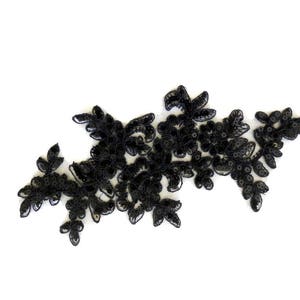 May include: Black lace applique with a floral design. The lace is delicate and intricate, with small sequins scattered throughout.