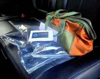 Könnte beinhalten: Eine durchsichtige Plastiktüte mit dunklen Gegenständen und einer weißen rechteckigen Karte mit der Aufschrift Contreptify 3D, neben einer orangefarbenen und olivgrünen Werkzeugtasche aus Segeltuch mit zwei Griffen, Reißverschluss und Fronttasche.