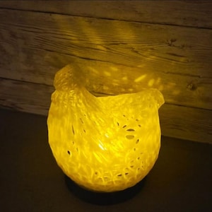 May include: A glowing yellow decorative bowl with a textured, woven appearance. The bowl is lit from within, casting a warm light and creating shadows on the wooden background. The bowl is sitting on a dark surface.