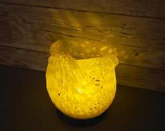 Könnte beinhalten: Eine leuchtend gelbe dekorative Schale mit einer strukturierten, gewebten Optik. Die Schale wird von innen beleuchtet, wirft warmes Licht und erzeugt Schatten auf dem Holzgrund. Die Schale steht auf einer dunklen Oberfläche.