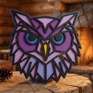 May include: A geometric owl wall art piece. The owl features a layered design with shades of purple, blue, and yellow, outlined in black. The owl's eyes are blue, and the beak is yellow. The artwork is displayed on a wooden surface.