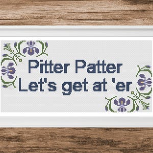 May include: A cross-stitch pattern in a white frame featuring the dark blue text Pitter Patter Let's get at 'er. The design is decorated with purple and green iris flower motifs on the left and right sides, set against a light gray background.