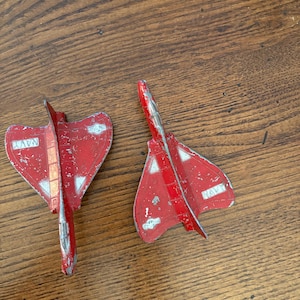 May include: Two vintage red toy airplanes with silver accents and the word "NAVY" printed on the wings. The toy planes are on a wooden surface and show signs of wear.