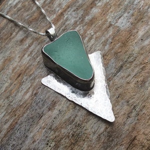May include: A silver necklace with a green sea glass pendant set in a hammered silver arrow shape.