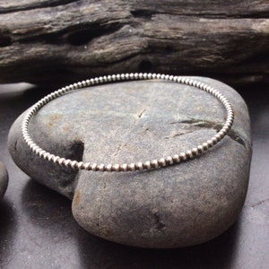 May include: A silver beaded bangle bracelet. The bracelet is made of small, round beads that are evenly spaced.
