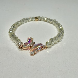 May include: A beaded bracelet featuring small, translucent, faceted light-green beads and a central butterfly-shaped charm. The butterfly charm is crafted from iridescent, multi-coloured crystal-like material set in a gold-toned metal frame.