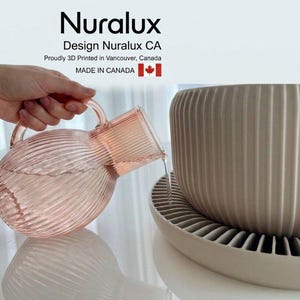 May include: A translucent pink ribbed glass pitcher with a handle pouring water into a matte beige ribbed planter with a matching saucer. Text at the top reads Nuralux, Design Nuralux CA, Proudly 3D Printed in Vancouver, Canada, MADE IN CANADA.