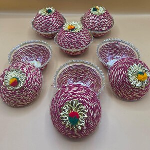May include: A set of decorative bowls and lids, handcrafted with a woven burgundy material and gold thread. Each lid features a gold floral embellishment with green and red accents. The bowls are designed for decorative purposes.