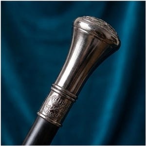 May include: A silver-toned walking cane with a dark wooden shaft. The handle features a decorative, engraved design and a rounded top. The cane is set against a blue background, highlighting its metallic sheen.