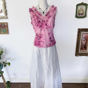 May include: A sleeveless pink floral top with a V-neck and a white skirt. The top features a pink floral pattern and lace trim. A black necklace is worn on the mannequin. The skirt is long and white.