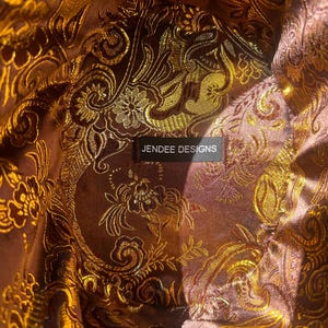 May include: Close-up of a brown fabric with a gold floral pattern. The fabric has a label that reads "Jendee Designs".
