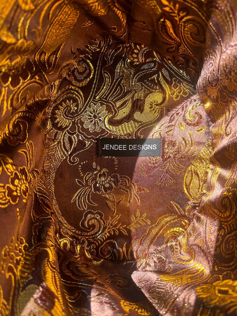 May include: Close-up of a brown fabric with a gold floral pattern. The fabric has a label that reads "Jendee Designs".