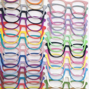 Puede incluir: Una colección de marcos de gafas de papel de colores brillantes, incluyendo morado, naranja, gris, negro, rojo, amarillo, azul, rosa, verde y marrón. Los marcos están dispuestos en filas, mostrando una variedad de estilos.