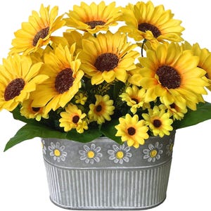 May include: A vibrant arrangement of yellow sunflowers with brown centers and smaller yellow flowers, set in a galvanized metal oval planter. The planter is decorated with daisy patterns around the rim, creating a cheerful floral display.