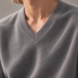 K&ouml;nnte beinhalten: Ein mittelgrauer V-Ausschnitt-Pullover aus weichem, strukturiertem Strickstoff. Das Kleidungsst&uuml;ck verf&uuml;gt &uuml;ber einen gerippten V-Ausschnitt und lange &Auml;rmel und bietet einen schlichten, klaren Look mit einer durchgehend einheitlichen Farbe.