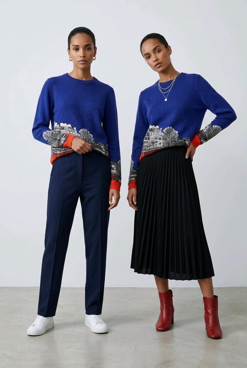 Puede incluir: Un su&eacute;ter azul de manga larga con un gr&aacute;fico de paisaje urbano en blanco y negro en la parte inferior del torso y las mangas, terminado con un dobladillo y pu&ntilde;os de color naranja vibrante. El su&eacute;ter se combina con pantalones azul marino o falda.