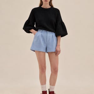 May include: A black ribbed knit sweater with voluminous sleeves, light blue tailored shorts with a front pleat and cuffed hem, sheer white ankle socks, and dark red lace-up leather boots with a thick sole and a rounded toe design.
