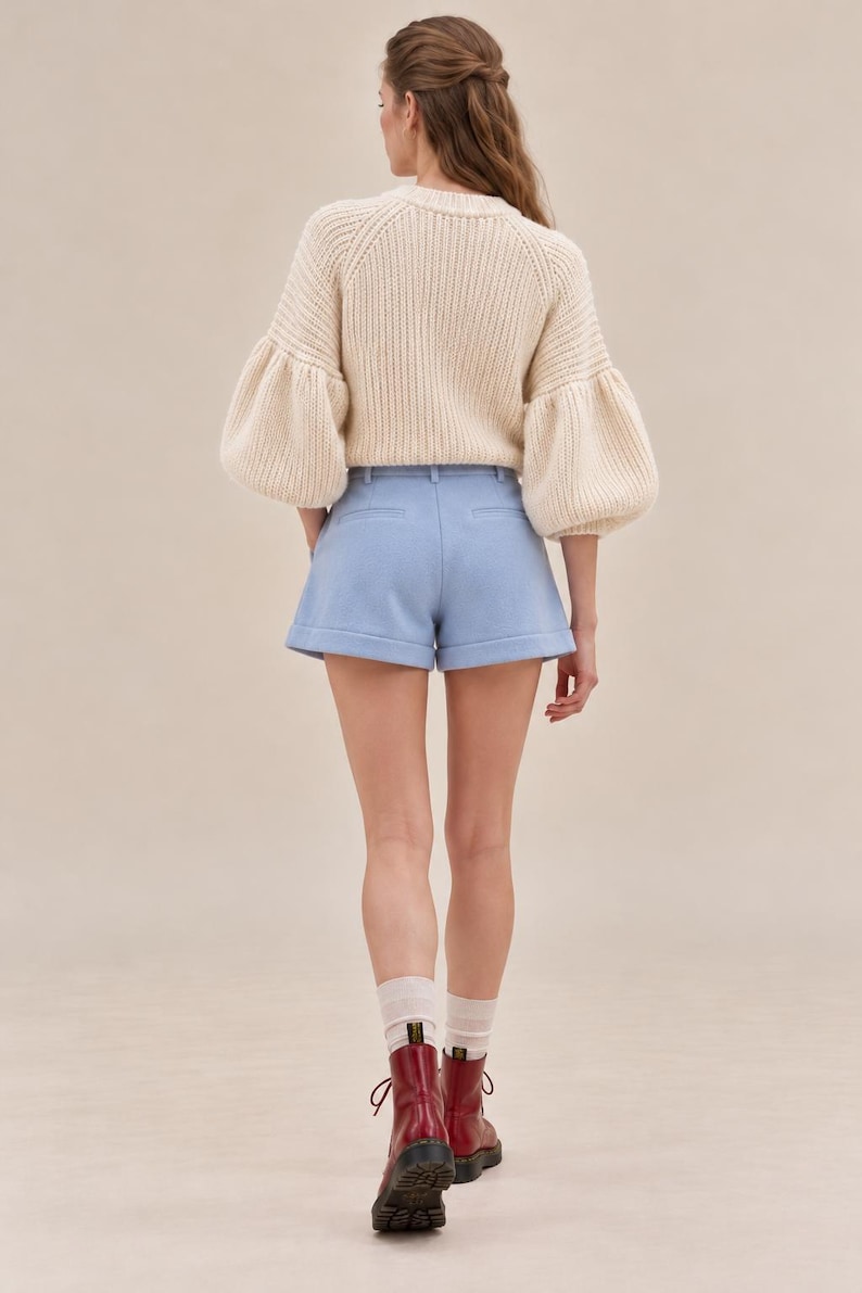 K&ouml;nnte beinhalten: Ein cremefarbener Rippstrickpullover mit volumin&ouml;sen langen &Auml;rmeln kombiniert mit hellblauen, ma&szlig;geschneiderten Shorts mit umgeschlagenem Saum, getragen mit transparenten wei&szlig;en Socken und dunkelroten Schn&uuml;rstiefeln aus Leder mit schwarzen Sohlen.