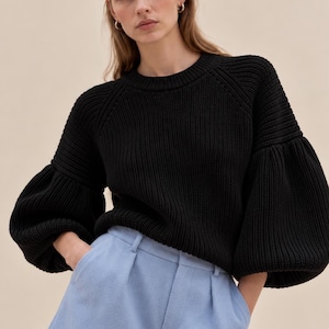 May include: A black long-sleeved knit sweater with a crew neckline and voluminous puffed sleeves paired with light blue tailored shorts featuring a pleated front, a waistband with belt loops, and cuffed hems.