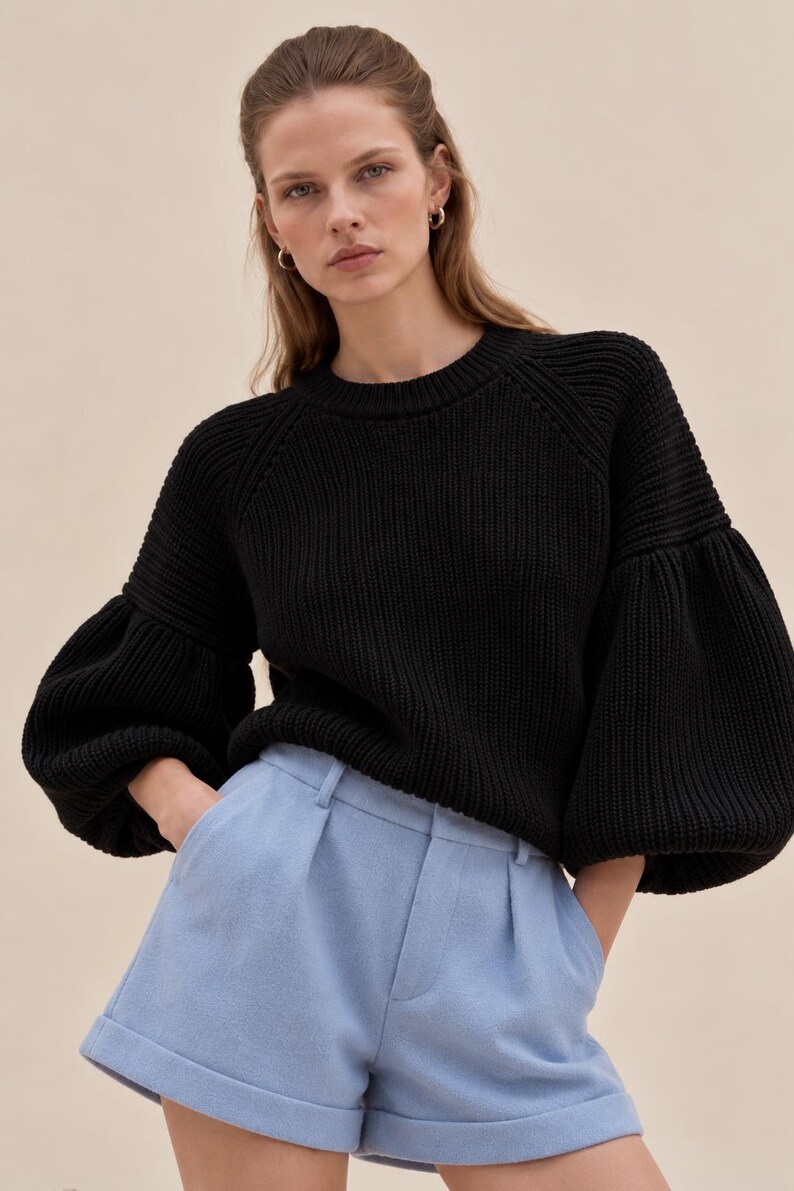 May include: A black long-sleeved knit sweater with a crew neckline and voluminous puffed sleeves paired with light blue tailored shorts featuring a pleated front, a waistband with belt loops, and cuffed hems.