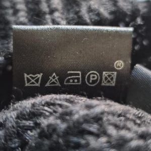 May include: A black fabric garment care label featuring five white laundry symbols: a crossed-out wash tub, a crossed-out triangle, an iron icon, a circle with the letter P, and a crossed-out square with a circle inside.